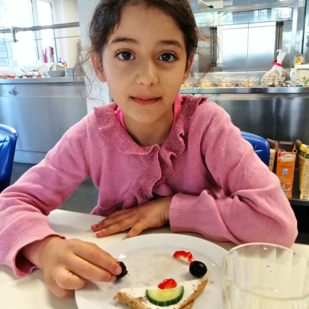Ein 7-jähriges Mädchen frühstückt Brot und Trauben und blickt in die Kamera.