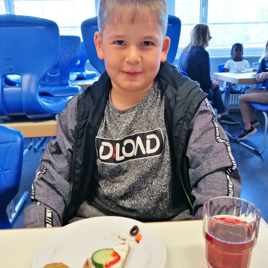 Armer Junge lächelt in die Kamera, während er frühstückt. Hilf mit deiner Spende benachteiligten Kindern in deiner Stadt