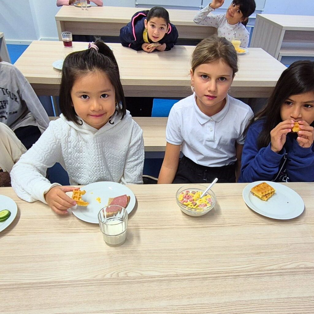 Drei Grundschülerinnen sitzen gemeinsam am gedeckten Tisch und freuen sich über Müsli und frisches Obst im Münchner Frühstücksklub.