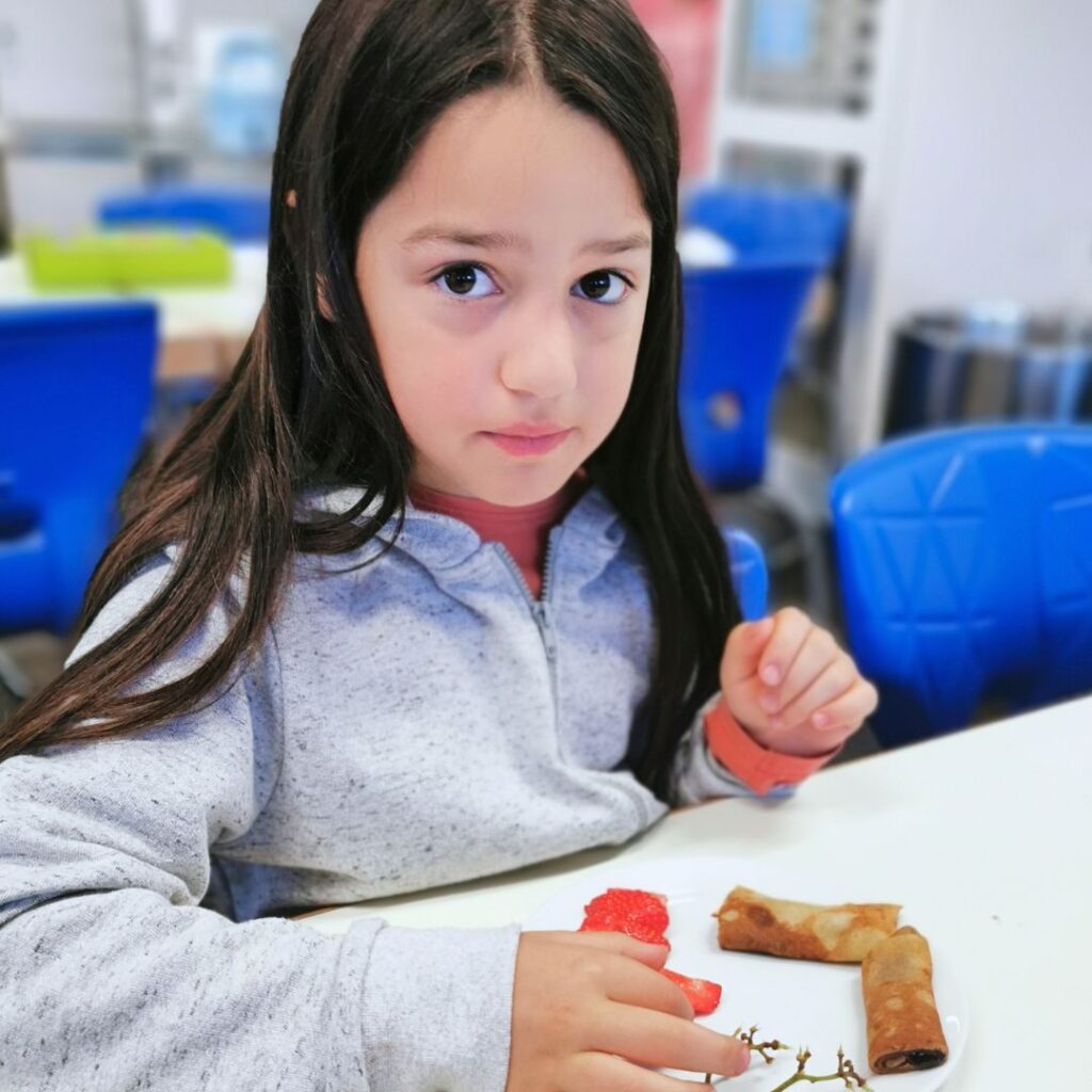 Mädchen frühstückt im Frühstücksklub der Deutschen Lebensbrücke e.V. in München-Obersendling und sitzt mit gesunden Snacks am Tisch.