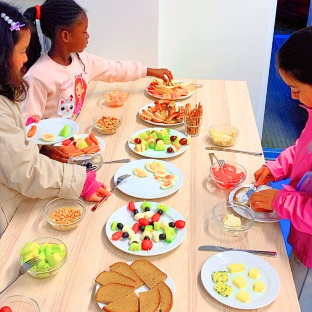 Kinder frühstücken gemeinsam im Frühstücksklub der Deutschen Lebensbrücke e.V. in München-Obersendling mit frischem Obst, Brot und gesunden Snacks.