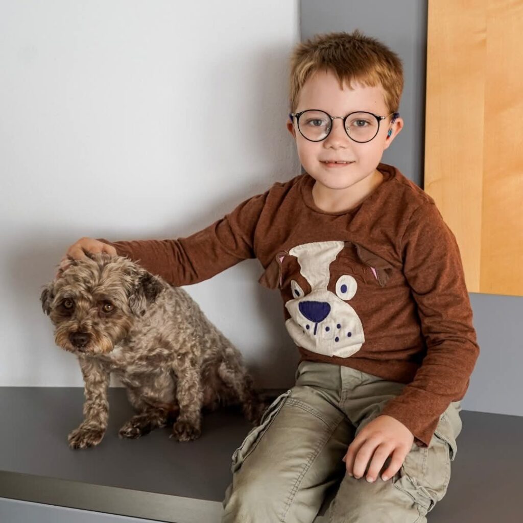 Silas sitzt neben einem kleinen Hund – ein ausgebildeter Assistenzhund soll dem siebenjährigen Jungen künftig Sicherheit und Halt geben.