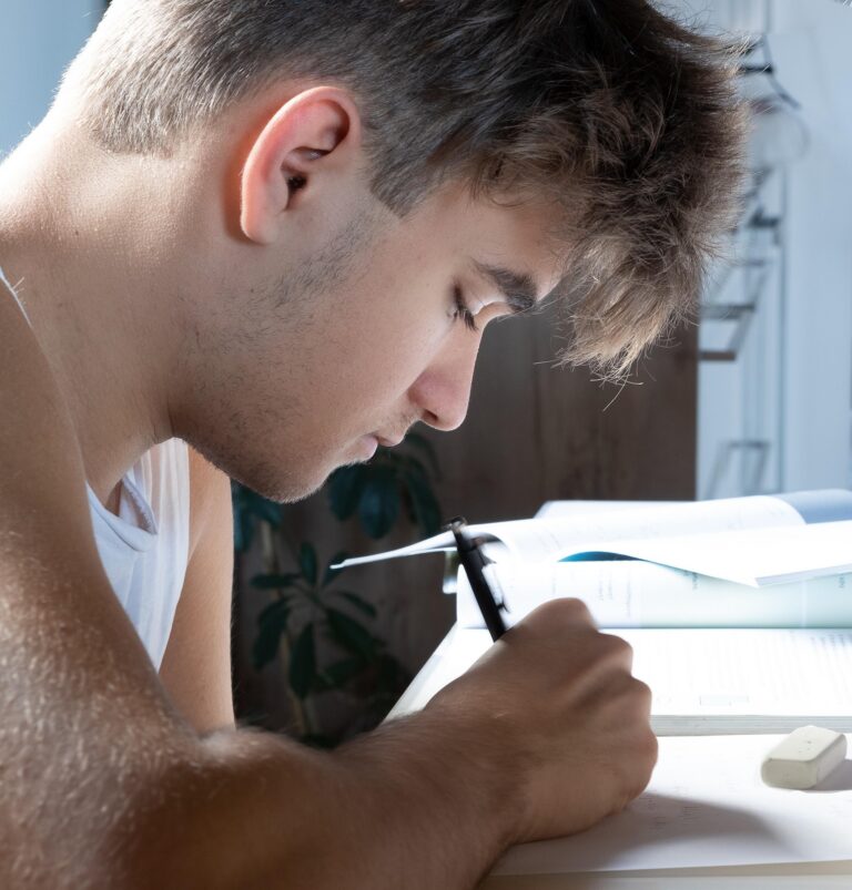 Junge sitz an Tisch vor Heften mit einem Stift in der Hand